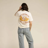 Person wearing a white t-shirt with a graphic and text, standing against a beige background