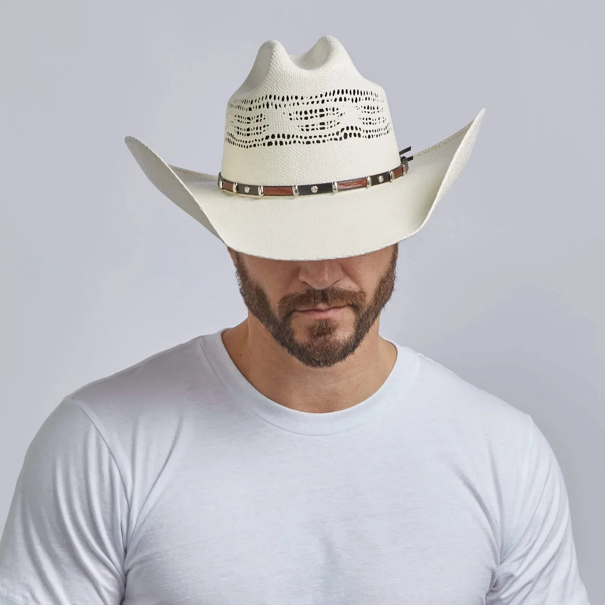 Man wearing a white cowboy hat with a brown band on a gray background